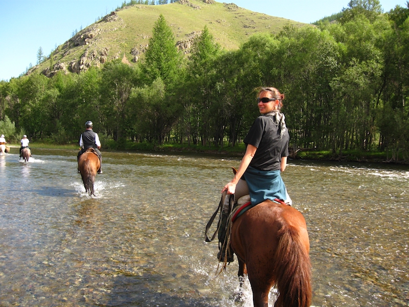 turisti in Mongolia guadano fiume durante un trekking a cavallo nel Parco Nazionale del Terelij